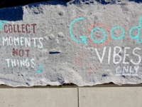 Collect Moments Not Things/Good Vibes Only, ghostly face, sun and hands. Chicago lakefront stone writings, between Belmont and Diversey Harbors. 2019