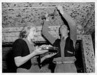 Vintage press photo: MIAMI, FLA: DEC-00-1940: The patience of Job, the friendliness of hundreds of delivery truck drivers as collectors and contributors has enabled Joe Wiser and his wife to build “Bottle Cap Inn” a bar in Miami at 1290 N. 119th St., whose walls and ceilings are decorated with over a million bottle caps. It took three years, a ton of nails and a ton of cement to do the job. Bottle caps are everywhere, on the floor, ceiling, bar, clock, lights, chairs, cash register, curtains, and even on the driveway. It’s the most unique rendezvous in Florida. Caps have been sent by admirers from the four corners of the world. Joe Wiser and his wife miss no opportunity to add to their collection. New bottle caps are as exciting to them as rare stamps to a philatelist. Here they are adding to their collection. This photo gratis for the City of Miami. Miami New Service, Hamilton Wright Jr., Executive Editor.