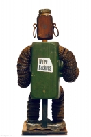 Seated green bottle-cap figure with Green Bay Packers helmet on chest, rear view with We're Backers written on back - vernacular art