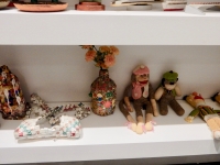 The bottom shelf from Chicago We Own It, center: Stanley Szwarc steel boxes, tramp art box, Harvey Ford sculpture, William Warmack bra, collaged jug, sock monkeys, crocheted Bert muppet dolls, monkey with cymbals, Nagua, Karl Wirsum Santa mask