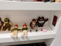 The bottom shelf from Chicago We Own It, right: sock monkey, crocheted Bert muppet dolls, monkey with cymbals, Nagua, Karl Wirsum Santa mask, needlepoint creature