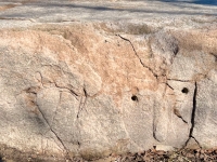 Triangle-bodied figure and face with square eyes and large nose, with Theater on the Lake in the background. Chicago lakefront stone carvings at Fullerton. 2019