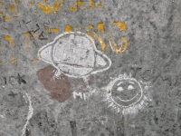 Smiling sun next to existing Saturn, AL 52, MR, Tom. Made at the June 20, 2026, DIY carving workshop. Chicago lakefront stone carvings, Promontory Point. 2026